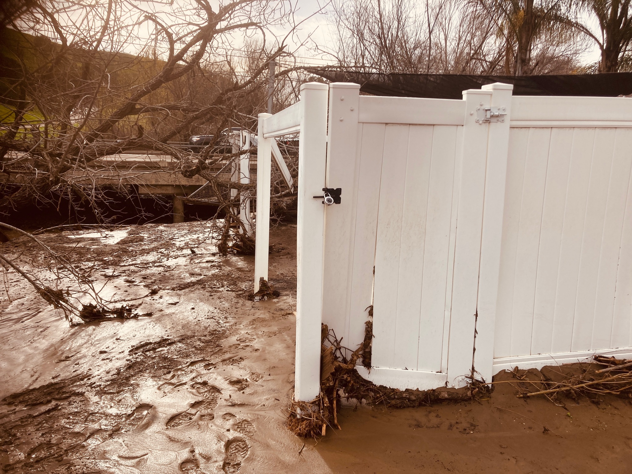 A white fence is encircled by muddy terrain and water